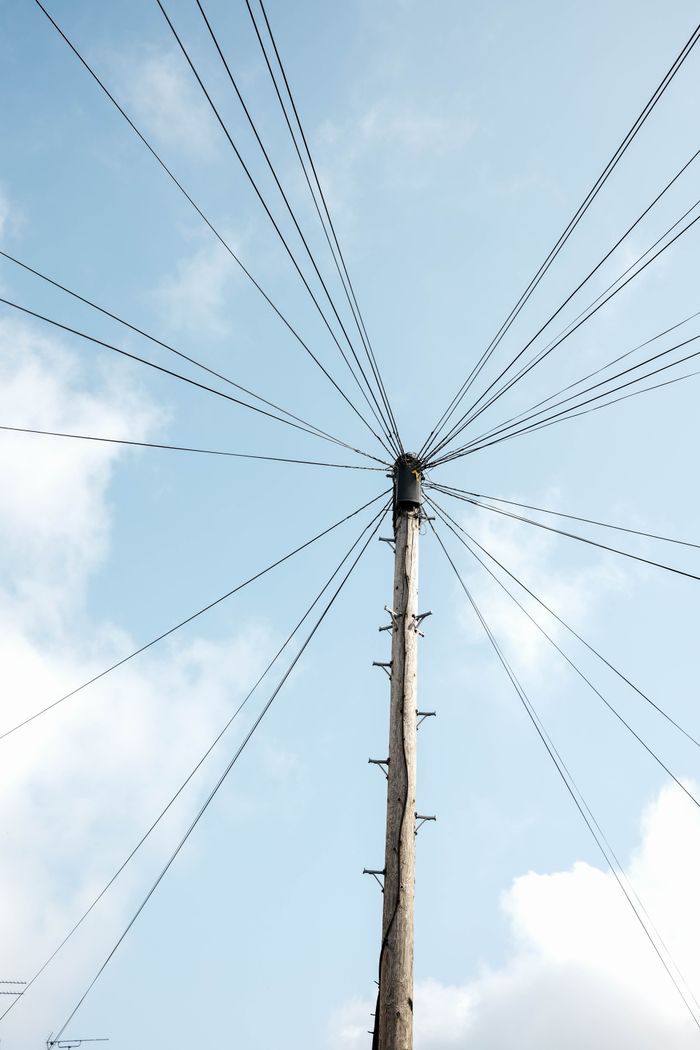 A wooden utility pole with cables extending into a clear blue sky, offering a minimalist perspective.