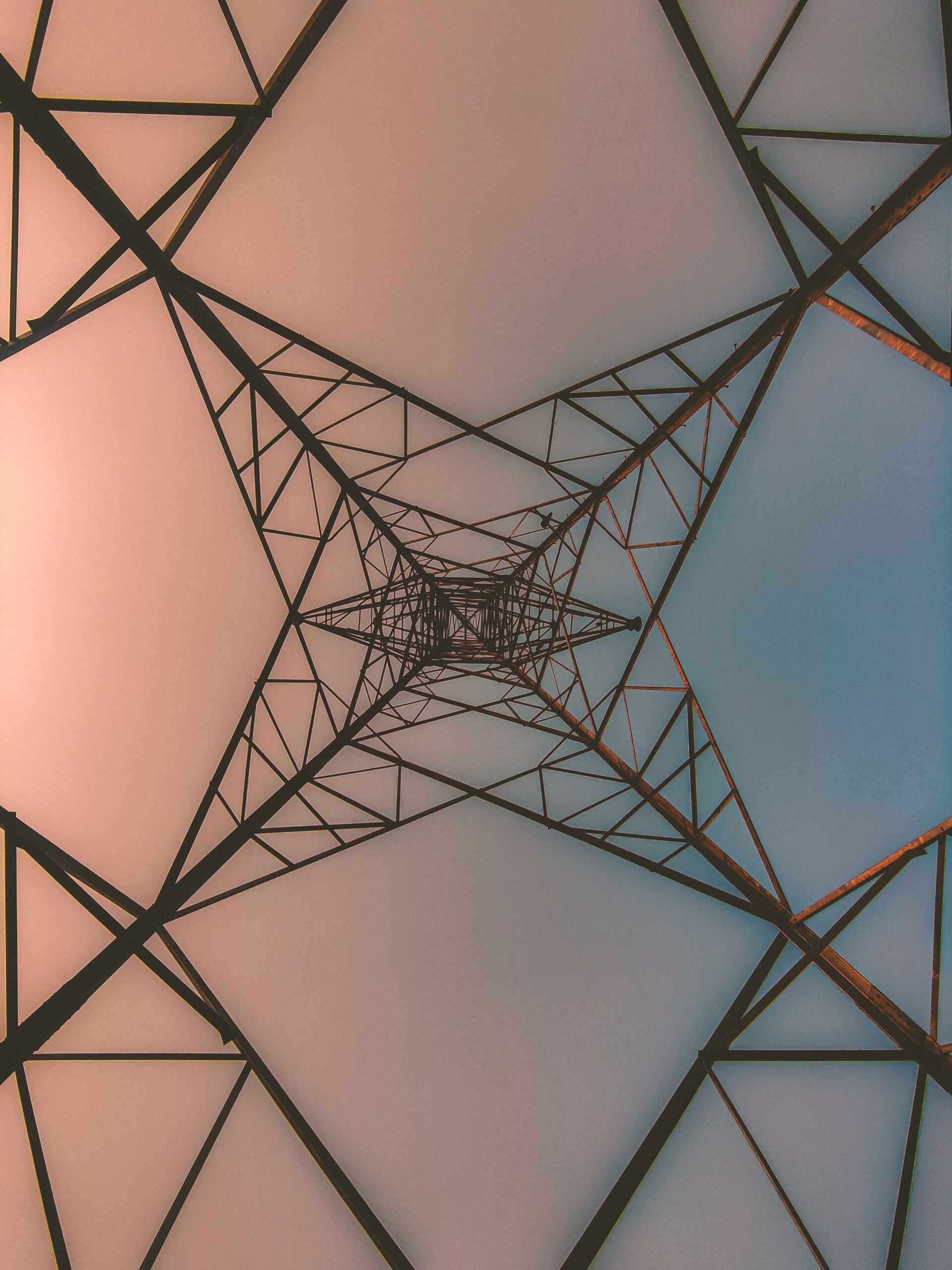 Artistic perspective of a steel tower against a pastel sky, viewed from below.