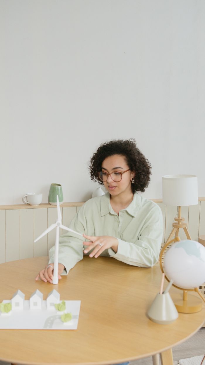 African American woman examining miniature wind turbine at a table, promoting sustainable energy.