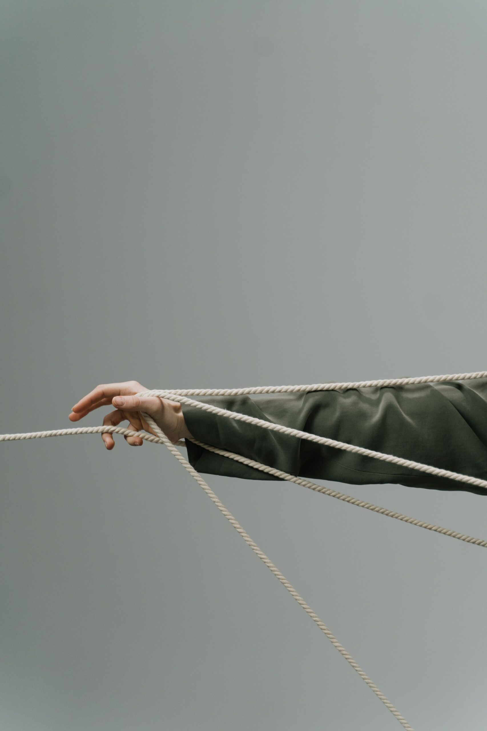 Artistic shot of a hand entangled in ropes against a gray background symbolizing stress and problems.